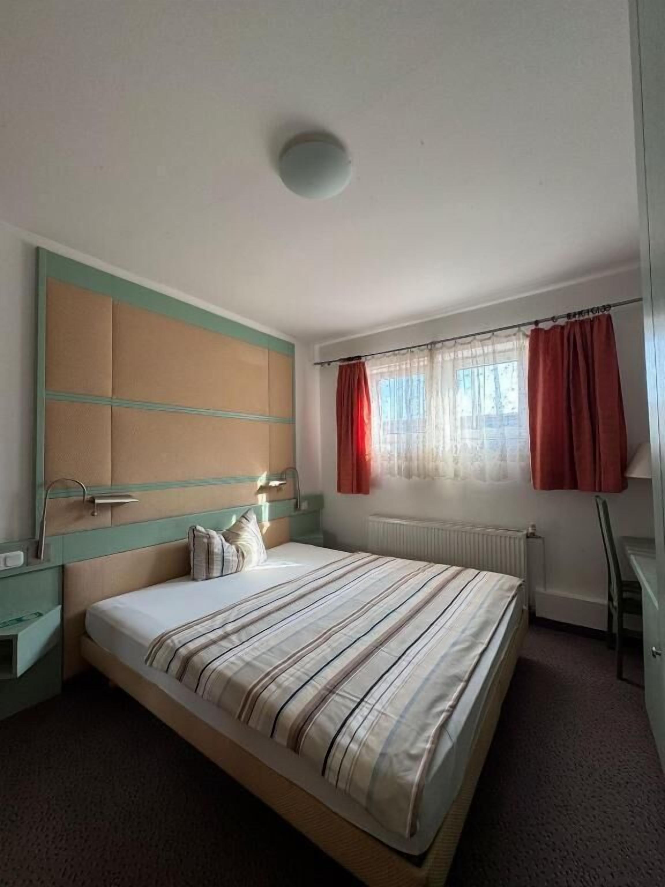 Ein Schlafzimmer mit einem Bett, einem Nachttisch, einer Kommode, einem Fenster mit Vorhängen und einer Heizung.