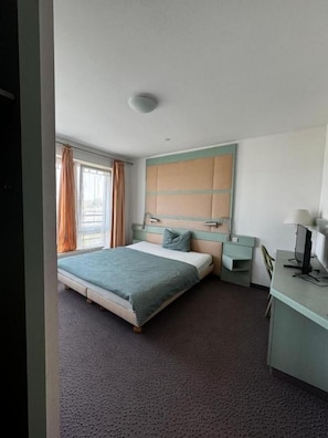 A hotel room with a bed, a desk, a chair, a lamp, and a window with curtains. - Hotel Route 84 (Bad Langensalza)