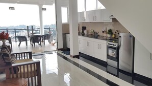 Una cocina moderna con armarios blancos, un refrigerador de acero inoxidable y un horno empotrado. Hay un balcón con mobiliario exterior y vistas a la ciudad.