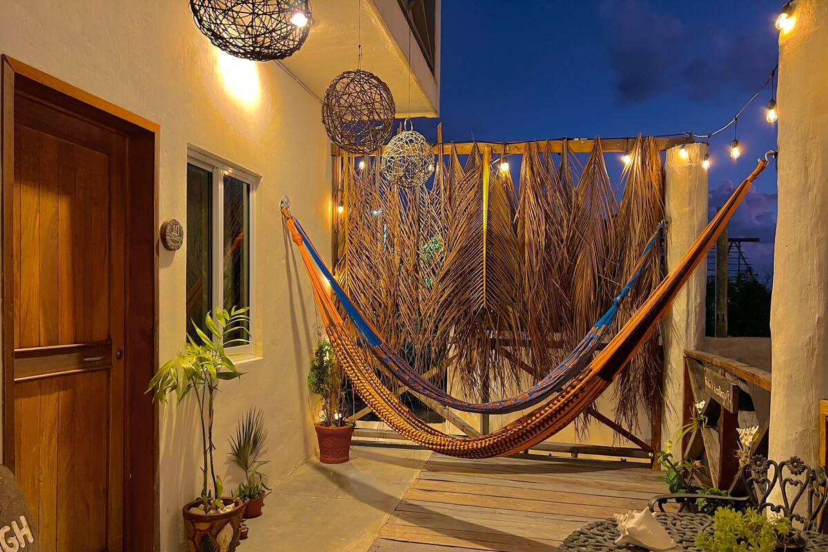 Un hamac dans une cour, agrémentée de plantes en pot et illuminée de guirlandes lumineuses.
