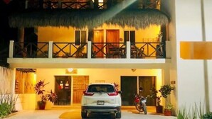Un edificio de dos pisos con techo de paja, un balcón y un coche estacionado al frente.