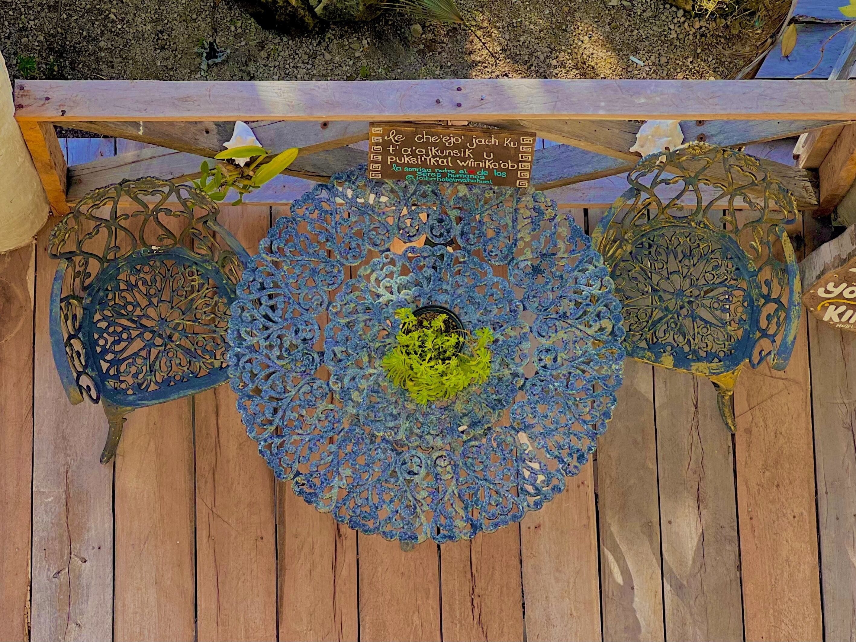 A wooden deck with three intricately designed metal chairs and a sign.