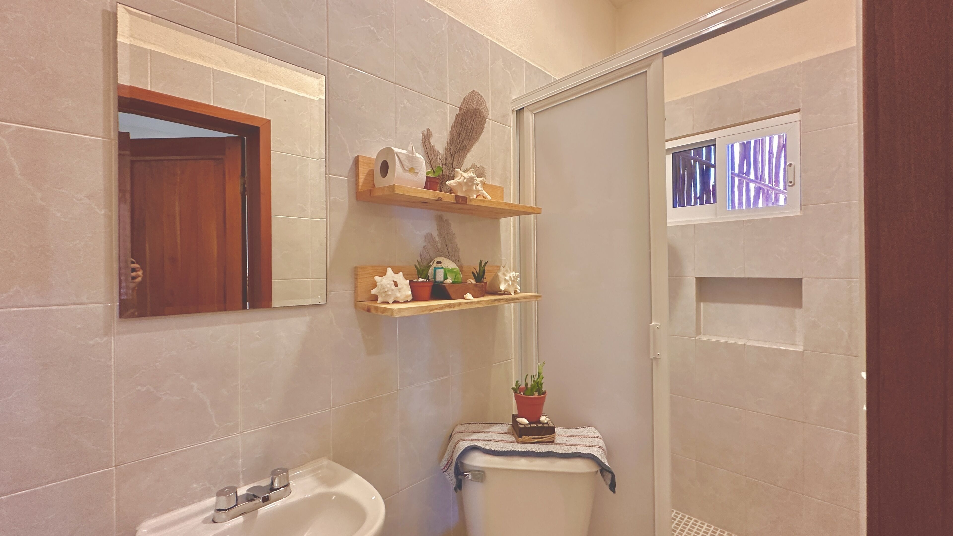 Een badkamer met een wastafel, spiegel en planken met toiletartikelen en decoratieve items.