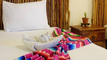 A hotel room with a bed, a white pillow, a colorful blanket, a wooden nightstand with a potted plant, and a wooden headboard.