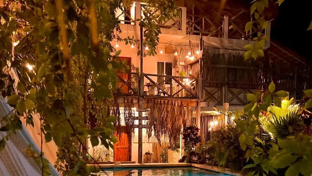 Piscina rodeada de exuberante vegetación y un edificio de estilo rústico.
