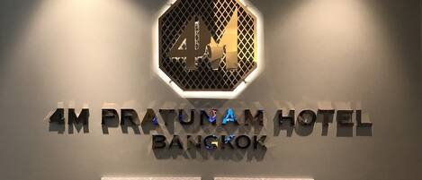 Een hotelschild met '4M PRATUNAM HOTEL BANGKOK' en de slogan 'BREATHE BELIEVE CONCUR'.