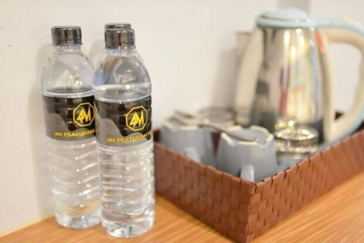 Two clear water bottles with a logo, a metal kettle, and a woven basket on a wooden surface.