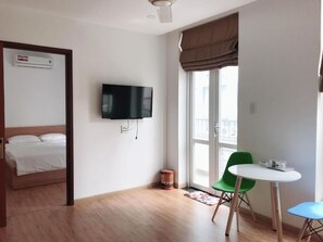 Ein Hotelzimmer mit Bett, Fernseher, Fenster mit Vorhängen, einem kleinen Tisch mit Stühlen und einer Klimaanlage.