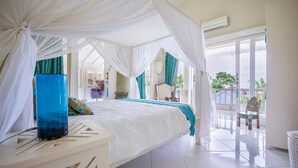 Un dormitorio con cama, mesita de noche, un florero azul y un balcón con sillas.