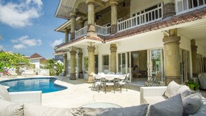 Una casa grande con piscina, muebles de exterior y un patio cubierto.
