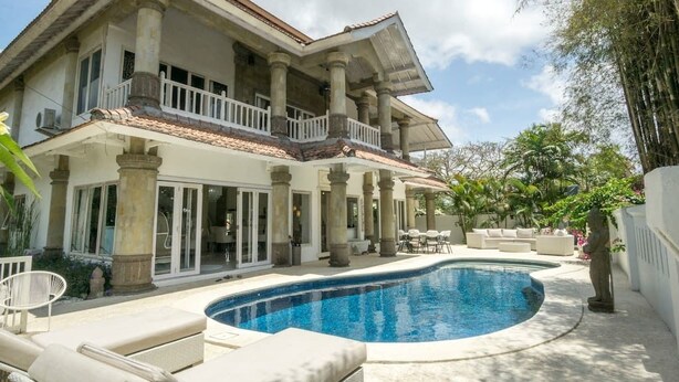 Una casa de dos pisos con piscina, mobiliario de exterior y jardín.