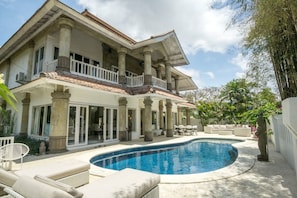 Una casa de dos pisos con piscina, mobiliario de exterior y jardín.