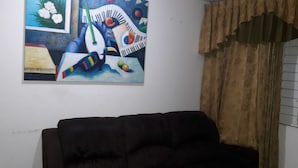 A living room with a dark-colored sofa, a painting on the wall, and a window with curtains. - Oaklands Apartment complex (Kingston)