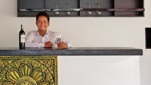 A bar area with a wine bottle and glasses on the counter, a decorative gold emblem on the wall, and a wine rack above. - Angkor Bosky Hotel (Siem Reap)