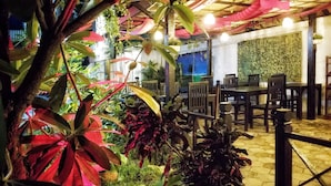 An outdoor dining area with tables and chairs, surrounded by lush greenery and a decorative wall. - Angkor Bosky Hotel (Siem Reap)