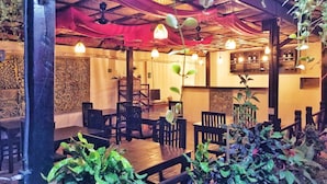 An indoor dining area with wooden tables and chairs, hanging plants, and decorative wall panels. - Angkor Bosky Hotel (Siem Reap)
