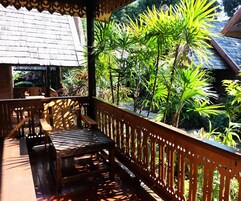 A wooden deck with a railing, surrounded by lush tropical plants.