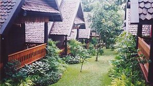 Uma fileira de edifícios em estilo tradicional com telhados de palha e guarda-corpos de madeira, cercada por vegetação exuberante e um gramado bem cuidado.