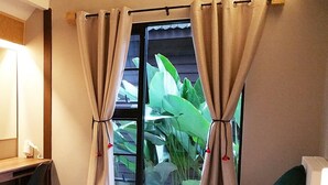 Quarto de hotel com cama, secretária com luminária, televisão e janela com cortinas.