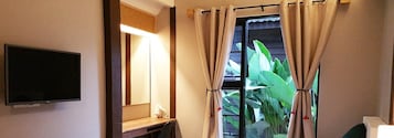 A hotel room with a bed, a desk with a lamp, a TV, and a window with curtains.