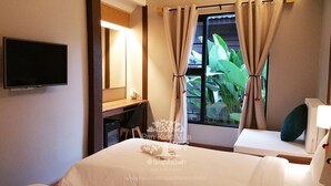 Quarto de hotel com cama, escrivaninha, cadeira, televisão e janela com cortinas.