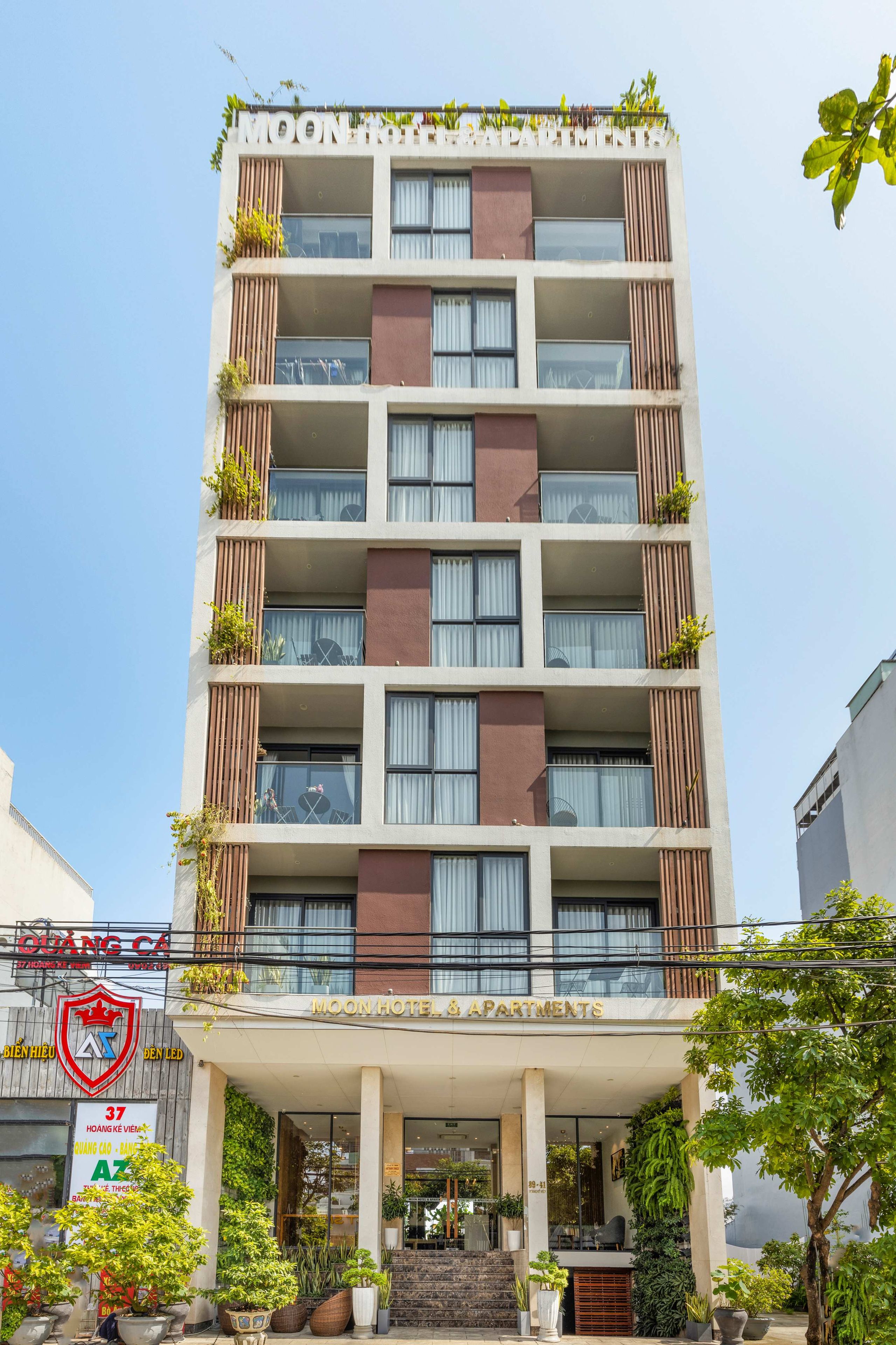 A multi-story hotel with balconies, a covered entrance, and potted plants.