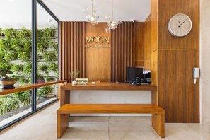 Un comptoir d’accueil avec un revêtement en bois, une enseigne indiquant « Réception », une horloge et une plante en pot.