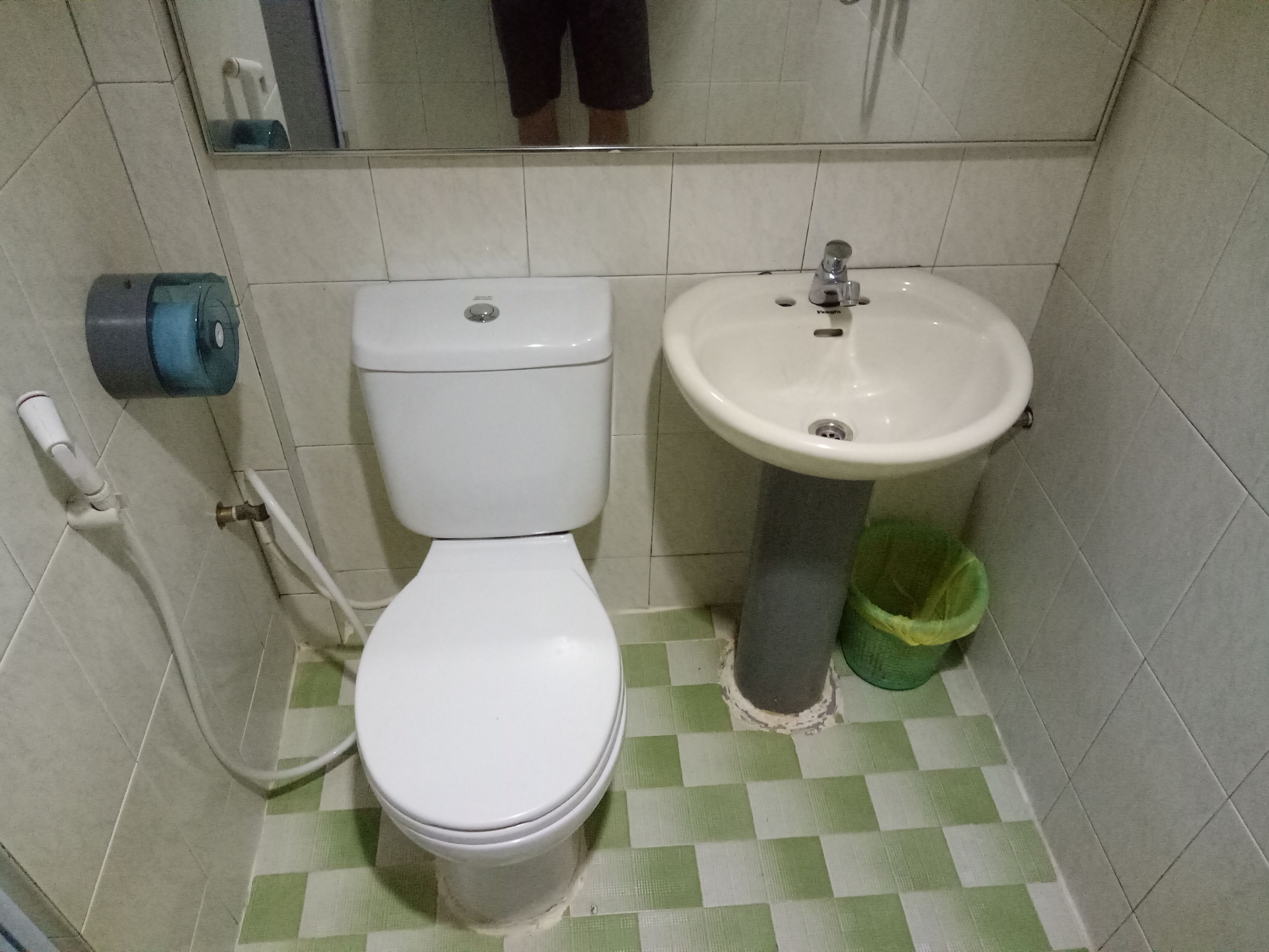 Un baño con inodoro, lavabo y un cubo de basura verde.