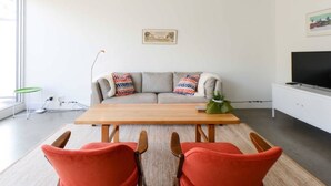 A modern living room with a sofa, two red chairs, a wooden table, and a television on a white cabinet. - StayCentral - Collingwood Penthouse (Collingwood)