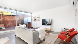 A modern living room with a large window, a sofa, a TV, and red chairs. - StayCentral - Collingwood Penthouse (Collingwood)