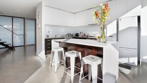 A modern kitchen with white cabinetry, a central island with stools, and a refrigerator. - StayCentral - Collingwood Penthouse (Collingwood)