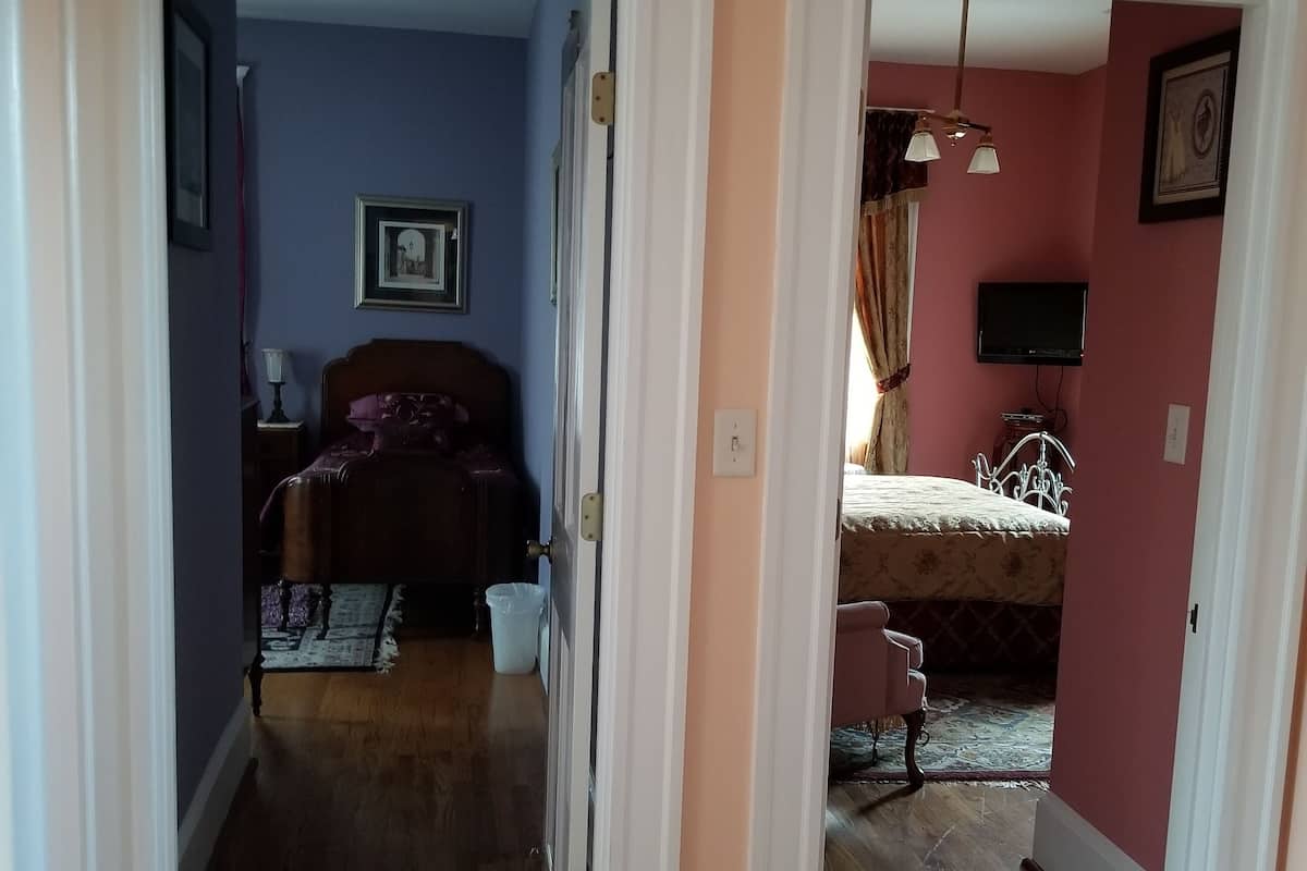 A hallway with a wooden floor leading to a bedroom with a bed and a dresser.