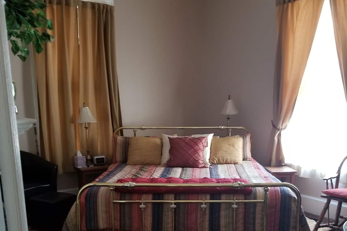 A hotel room with a bed, a chair, a desk, a lamp, and a window with curtains.