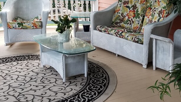 A porch with wicker furniture, a glass coffee table, and a patterned rug.