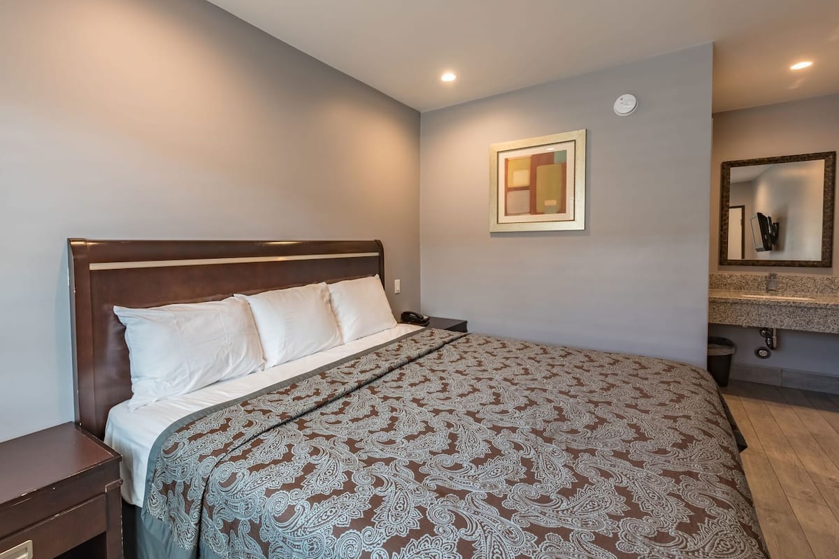 Quarto com cama, mesa de cabeceira e banheiro com pia e espelho.