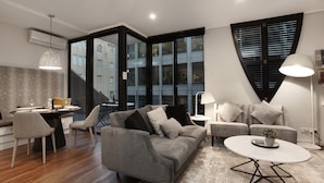 Una sala de estar moderna con un sofá gris, una mesa de centro redonda y un comedor con una mesa preparada para dos.