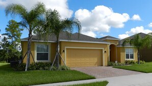 A single-story house with a yellow exterior, a garage, and a well-maintained lawn. - Sm215701 - Watersong - 5 Bed 4 Baths Villa (Davenport)