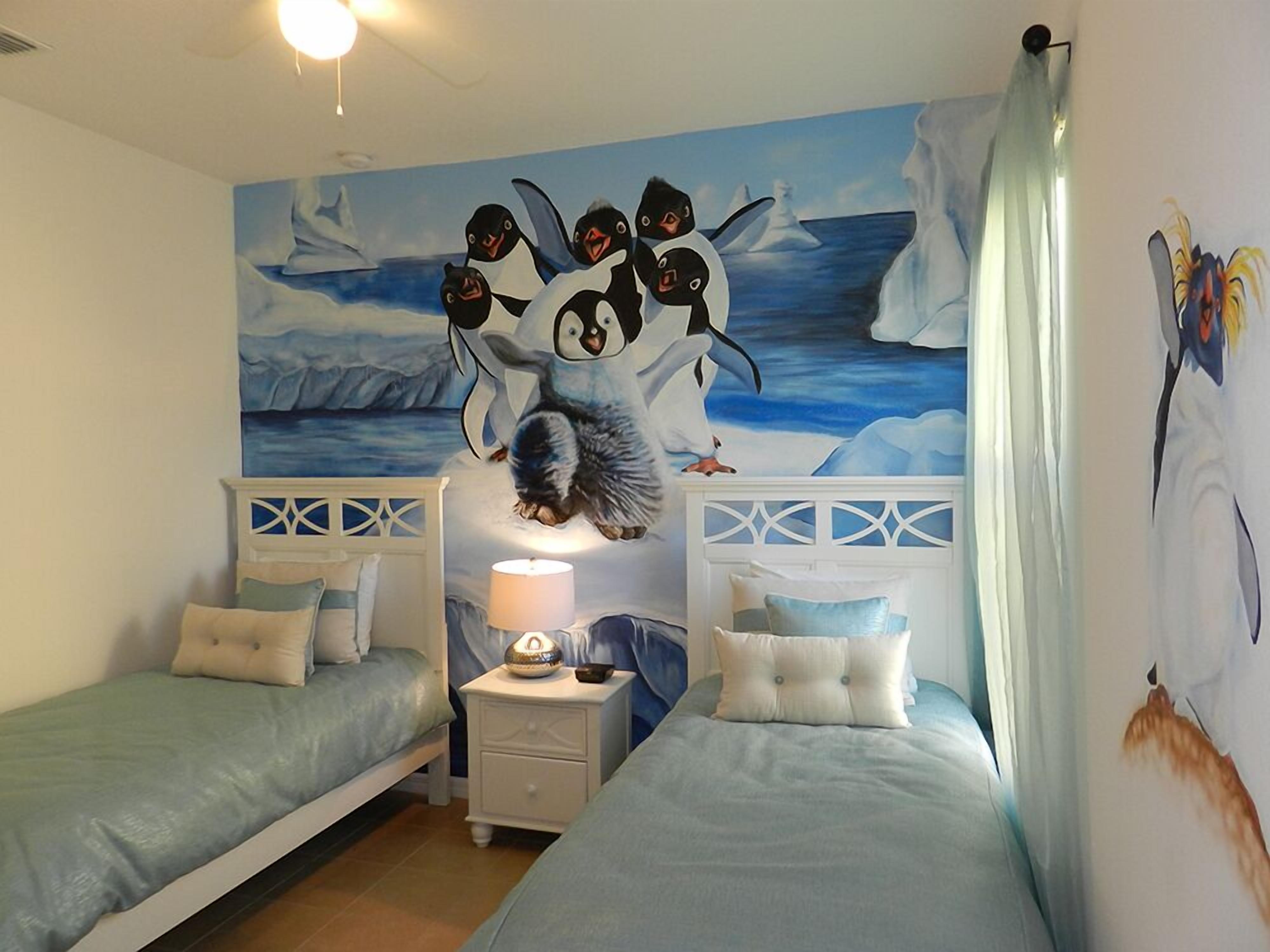 Un dormitorio con dos camas, una mesita de noche con lámpara y un mural de pingüinos en la pared.