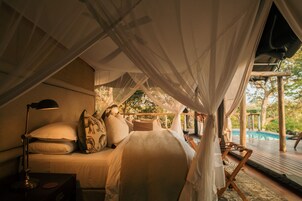 Quarto com cama, almofadas, luminária e vista para uma piscina ao ar livre.