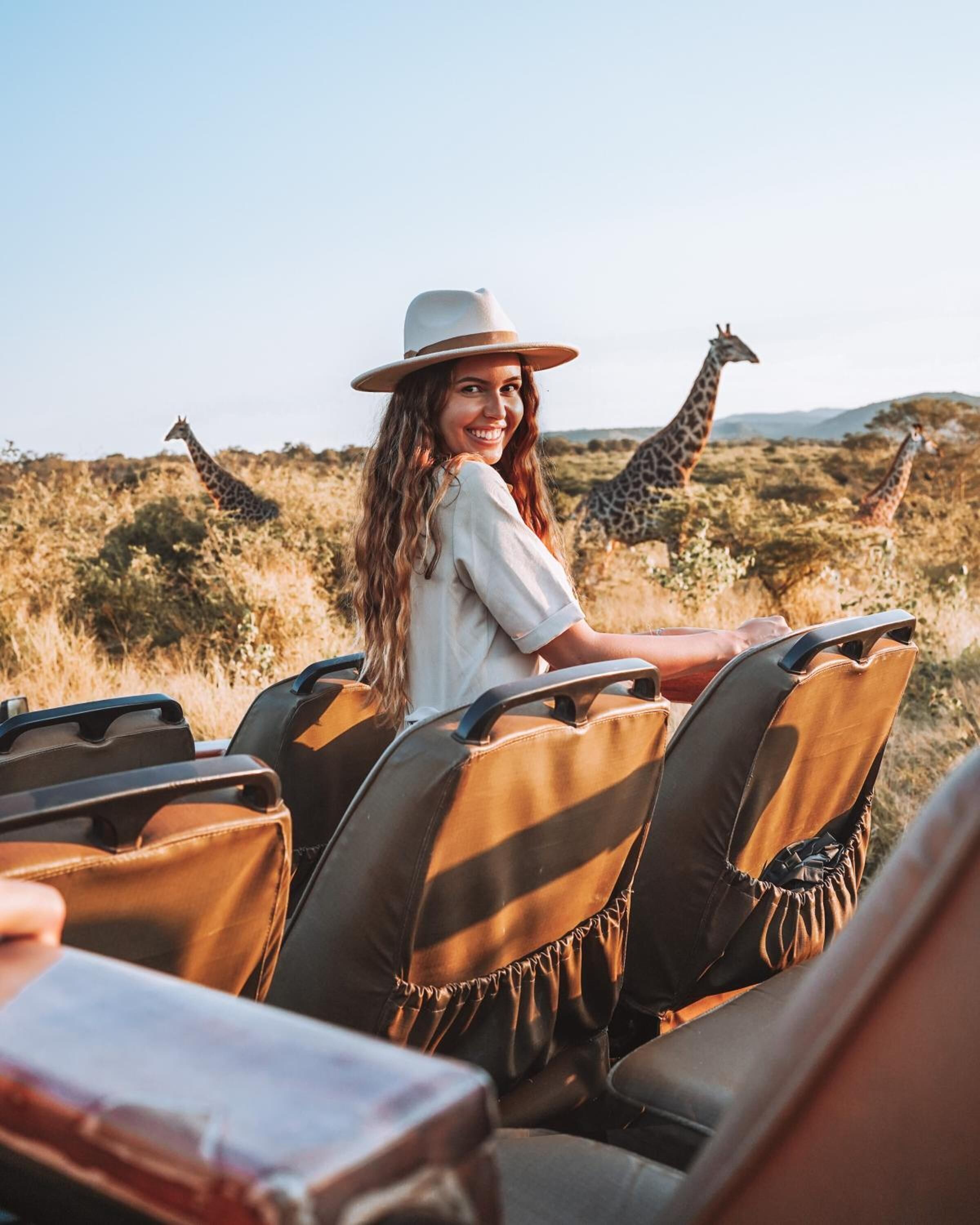 Une personne assise dans un véhicule de safari, avec des girafes en arrière-plan.