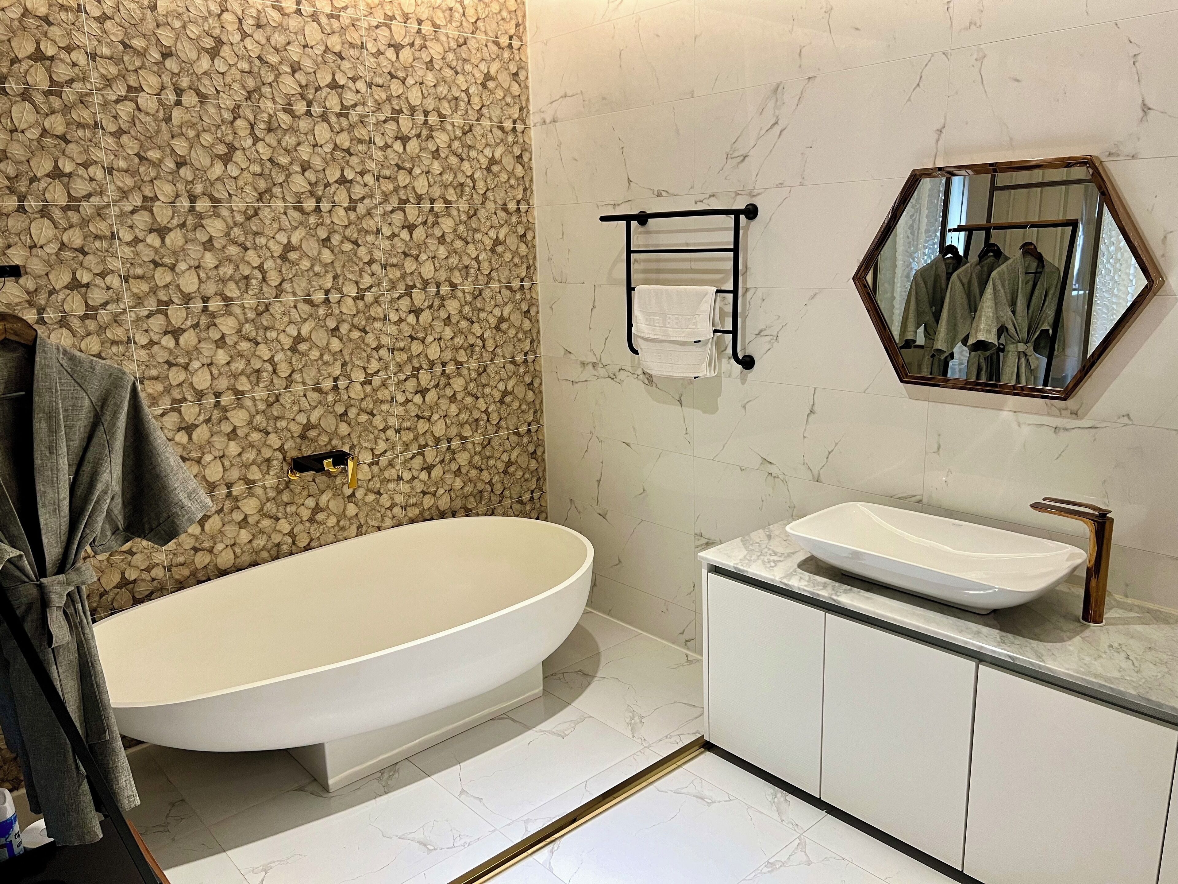 A modern bathroom with a freestanding bathtub, a large mirror, and marble flooring.