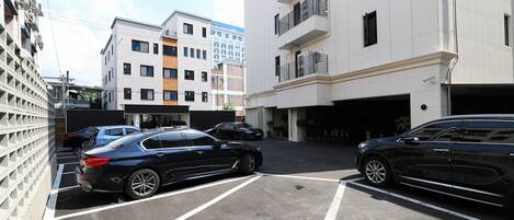 Un área de estacionamiento con dos coches negros estacionados en espacios designados, rodeada de edificios de varios pisos con balcones y la entrada a un garaje.
