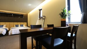 Ein Hotelzimmer mit zwei Betten, einem Esstisch mit Stühlen, einer Pflanze und einem Fenster mit Vorhängen.