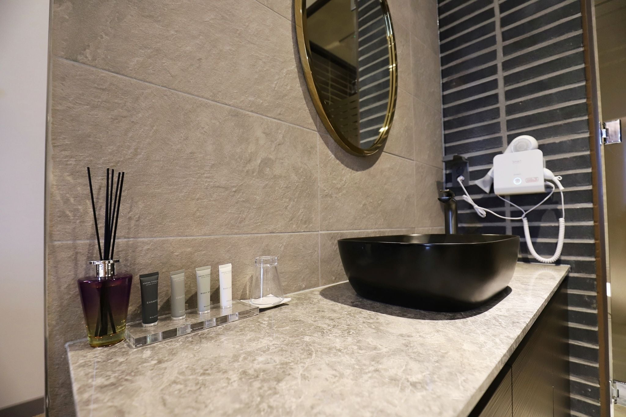 A bathroom with a large mirror, a black basin, and a hairdryer on the wall.