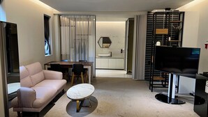 Ein modernes Hotelzimmer mit einer Couch, einem runden Couchtisch, einem Fernseher und einem Essbereich mit Tisch und Stühlen.