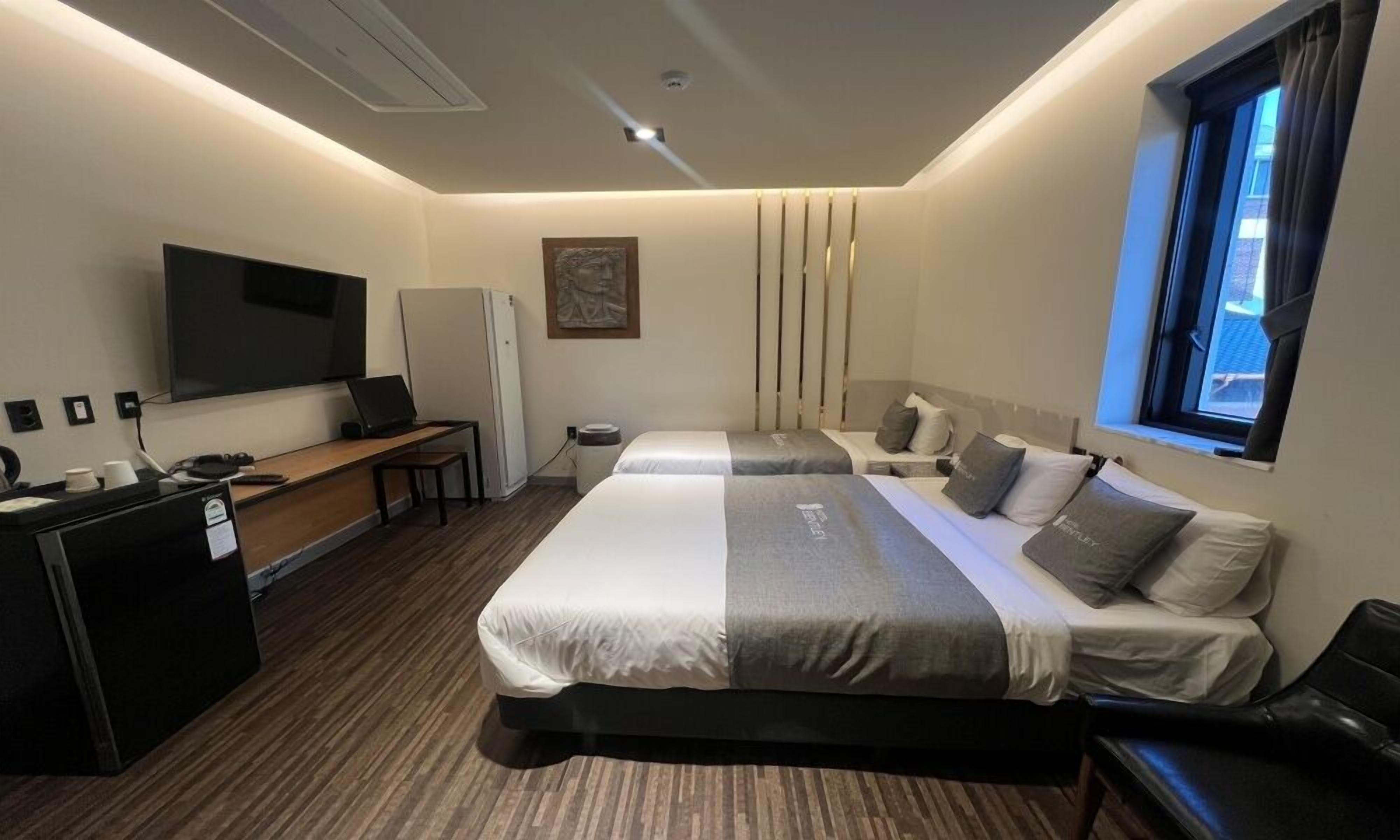 A modern hotel room with a large bed, a desk, a television, and a window.