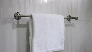 Una toalla blanca colgada en un tendedero de metal frente a una pared de azulejos.