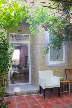 A patio area with a white chair, a small table, and a window with a purple frame.