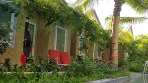 Un área junto a la piscina con un borde de piedra, una silla tapizada de rojo y abundante vegetación.