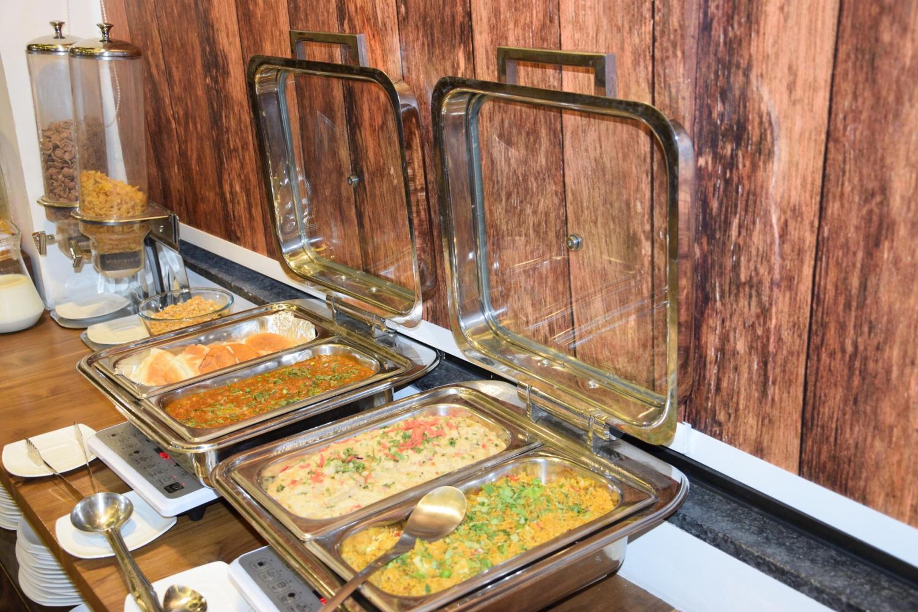 A buffet with various food items in metal serving trays, set against a wooden wall.